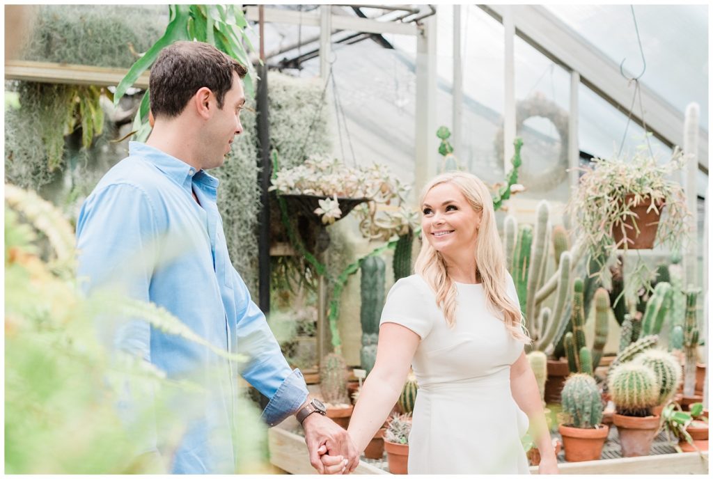 A couple holds hands walking through a greenhouse.