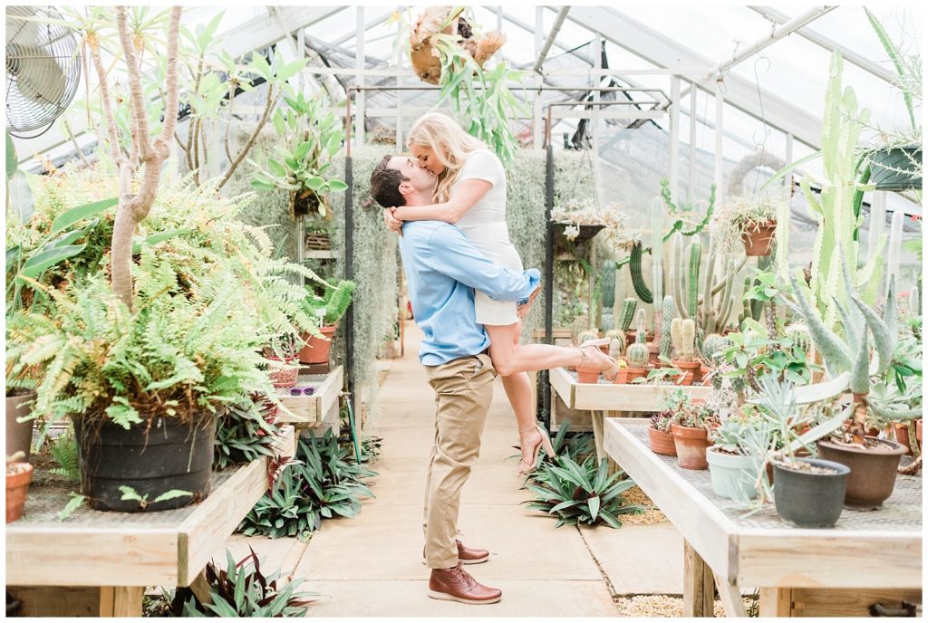 A man lifts up a woman inside a lush greenhouse in NJ.