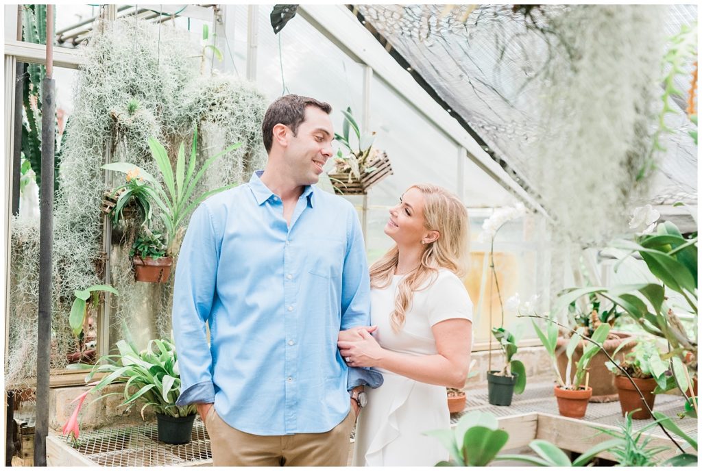 A couple looks at each other inside a greenhouse.