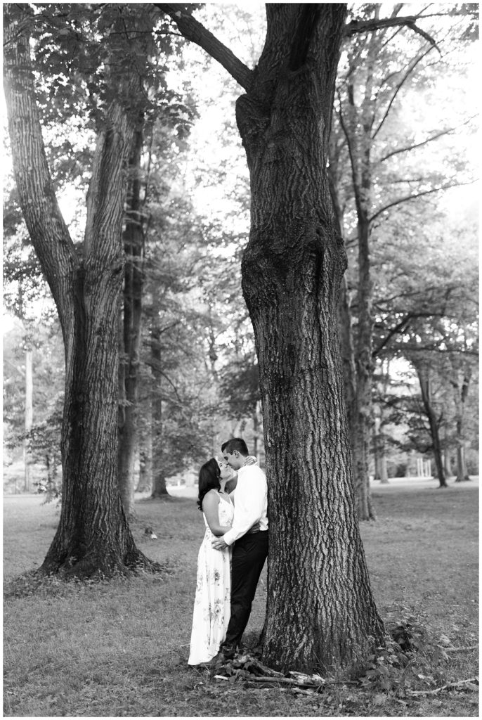A couple kisses while leaning on a tall tree.
