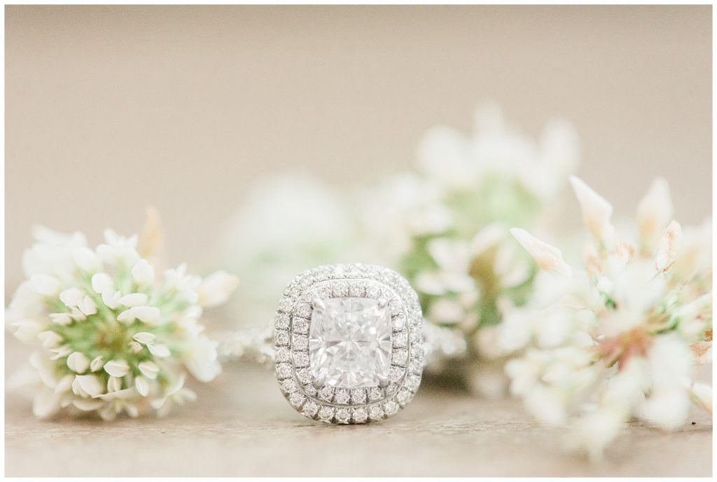 A diamond engagement ring sits among little white flowers.