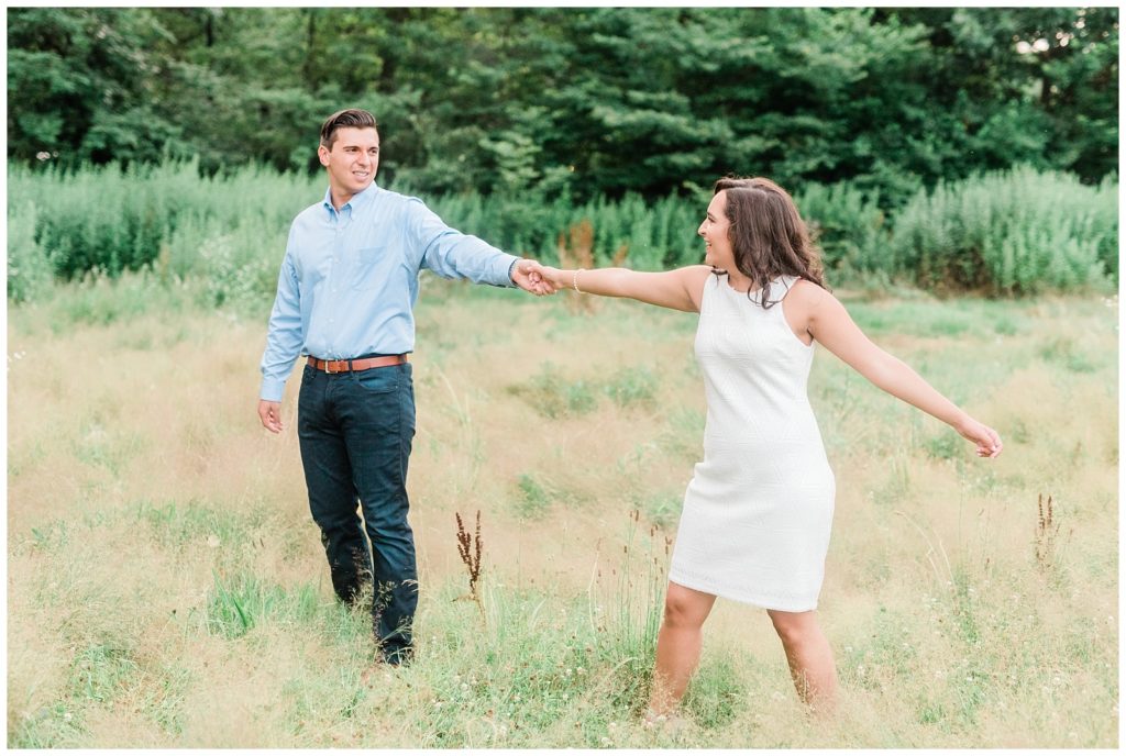 A couple holds hands twirling in a field of tall grass in Brookdale Park.