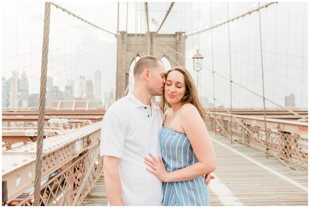 Man kisses his fiance on the cheek on the Brooklyn Bridge.