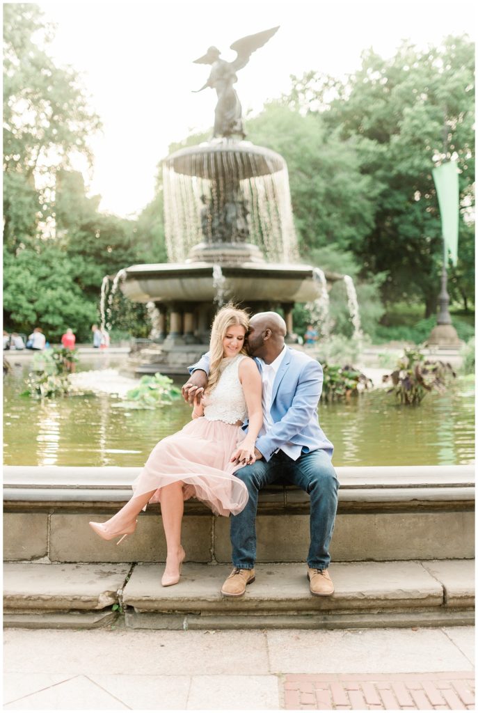 A couple sits on the edge of Bethesda Fountain wrapping each other in a big hug.