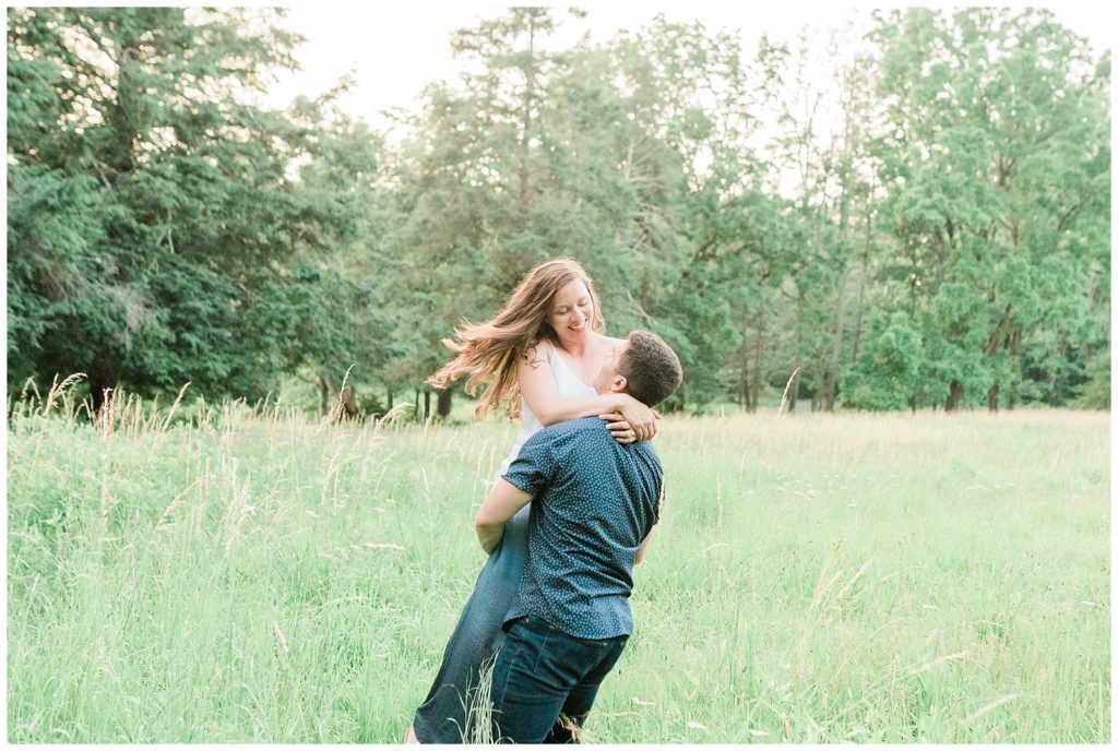 A man spins his fiancee around in a field of tall grass.