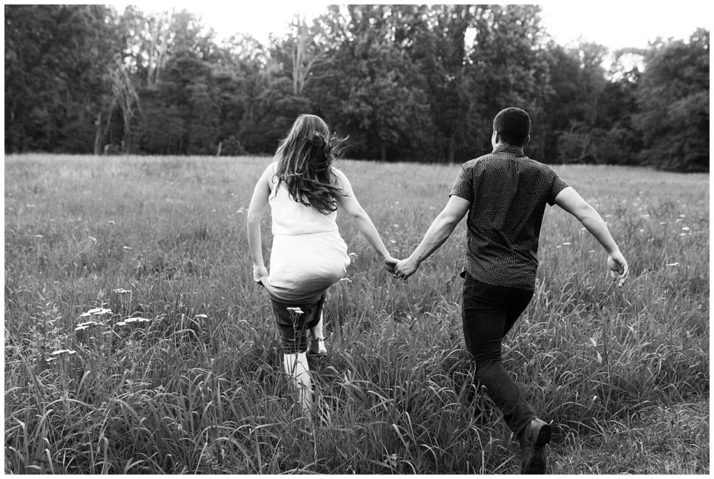 A couple holds hands running through a field of tall grass.