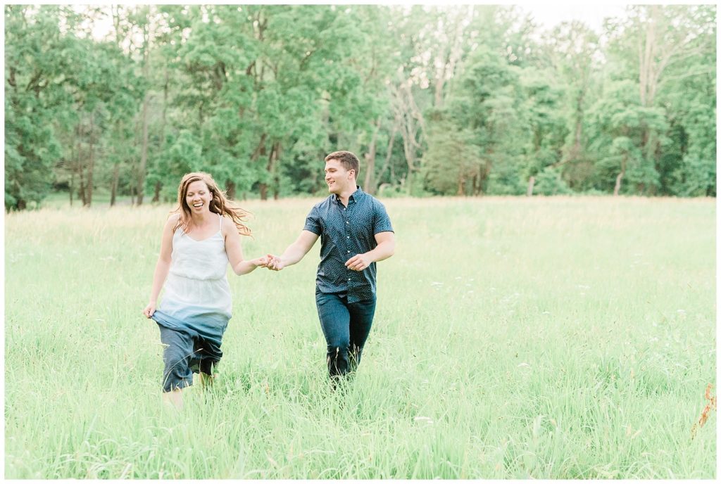 A couple holds hands running through a field of tall grass together.