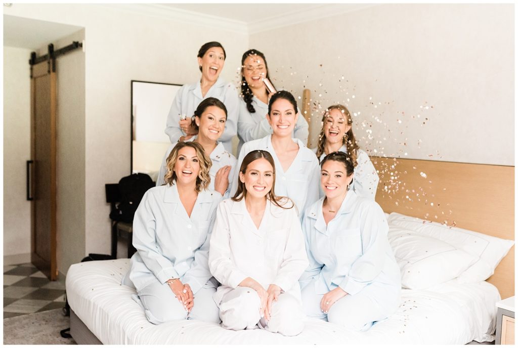 A bride and her bridesmaids pop confetti on a bed.