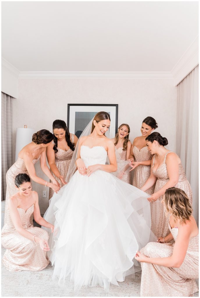 Bridesmaids help the bride with her wedding gown.