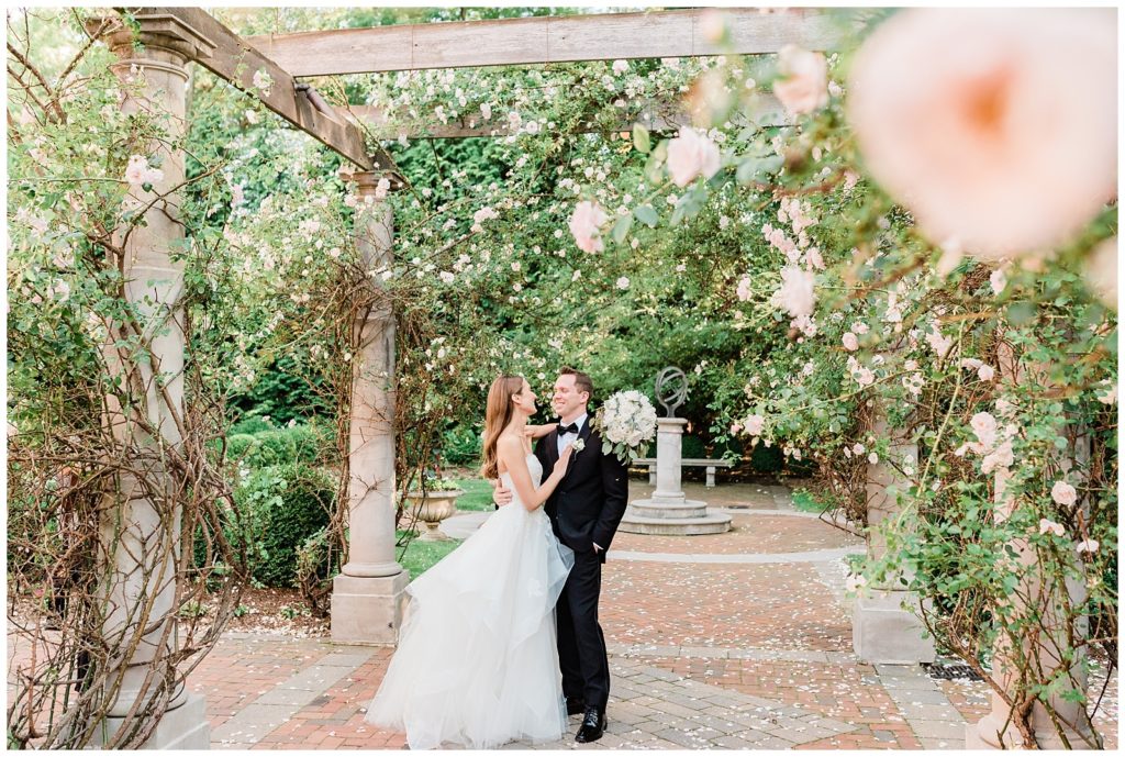 A bride and groom dance beneath a rose covered pergola.