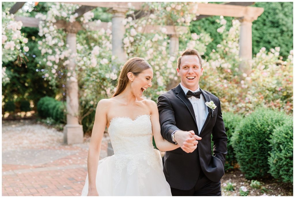A bride and groom hold hands walking and laughing in the roses at Florentine Gardens.