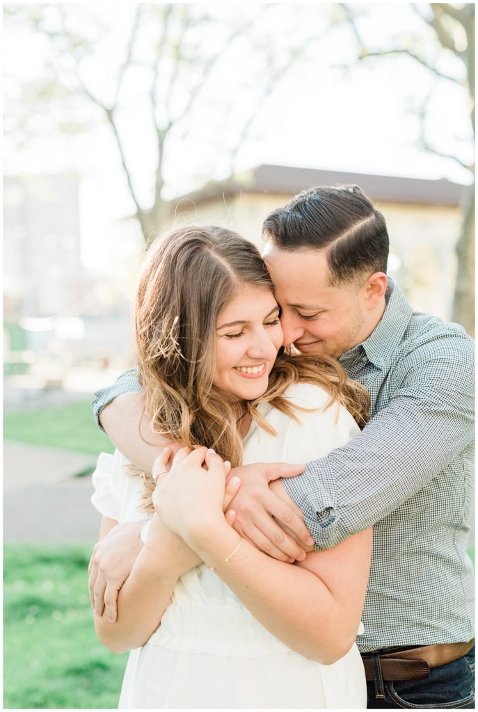 Man hugs his fiance from behind while smiling.