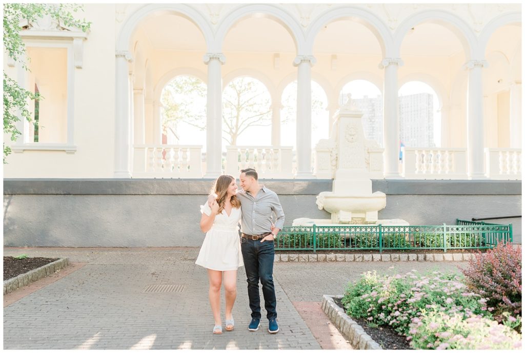 A couple walks together in front of an arched gazebo in Hoboken.