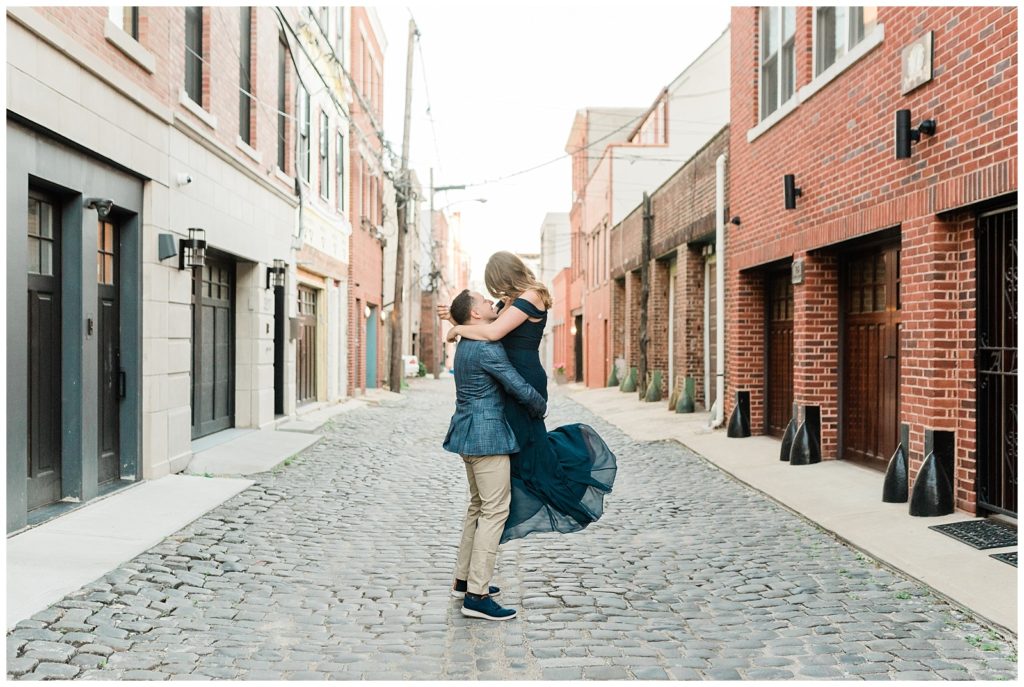 A man lifts up his fiance on a cobblestone street in Hoboken, NJ.