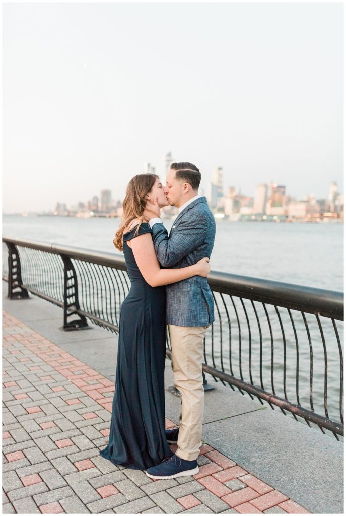 A couple kisses in front of the NYC skyline at the Hoboken waterfront.
