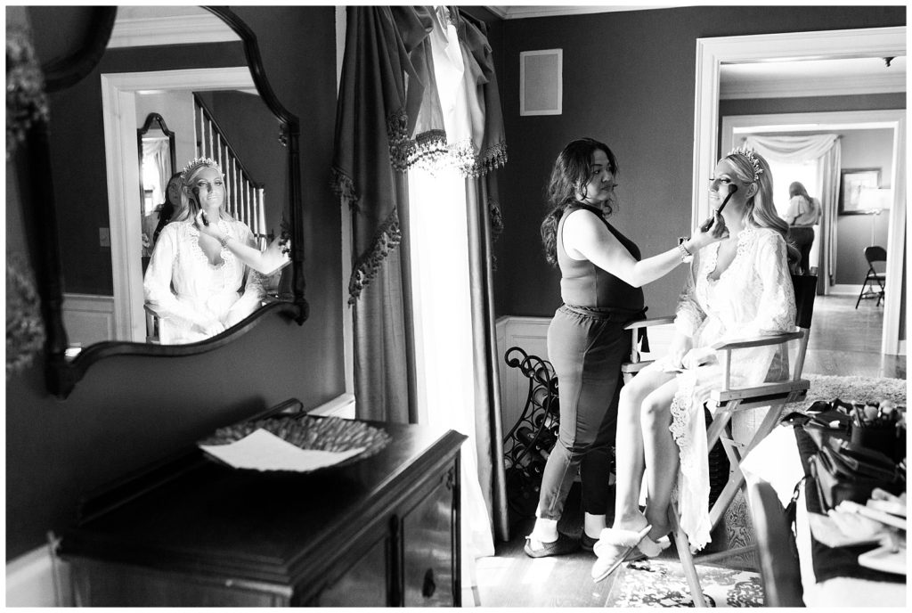Make me up eva does makeup on the bride in her home, with a reflection of the bride in the mirror.