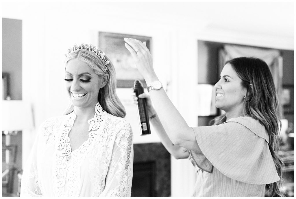 Boho hair salon stylist sprays hairspray on the bride's hair to finish her wedding day look.