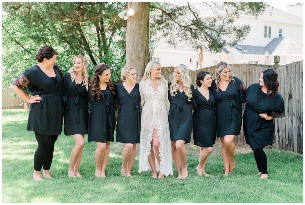 A bride poses for a photo with her bridesmaids while wearing robes in the backyard.