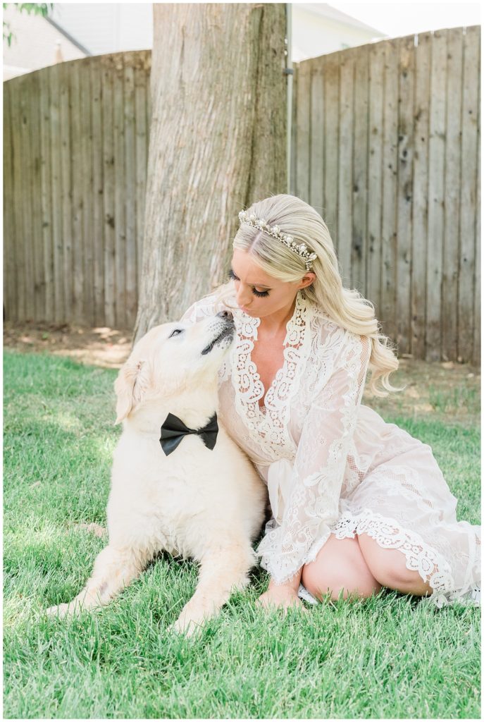 The bride sits with her dog in the backyard while wearing her wedding day robe.