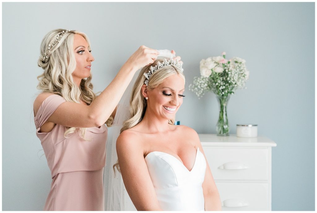The maid of honor puts the veil into the bride's hair.