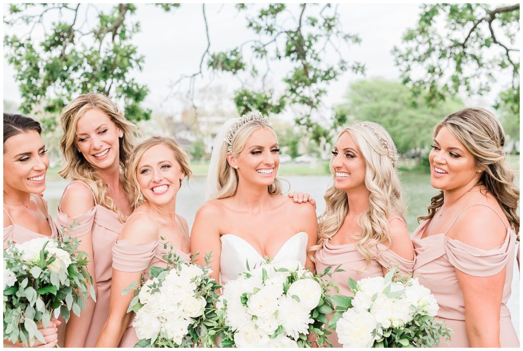 A bride and her bridesmaids smile and laugh together while holding white peony bouquets.