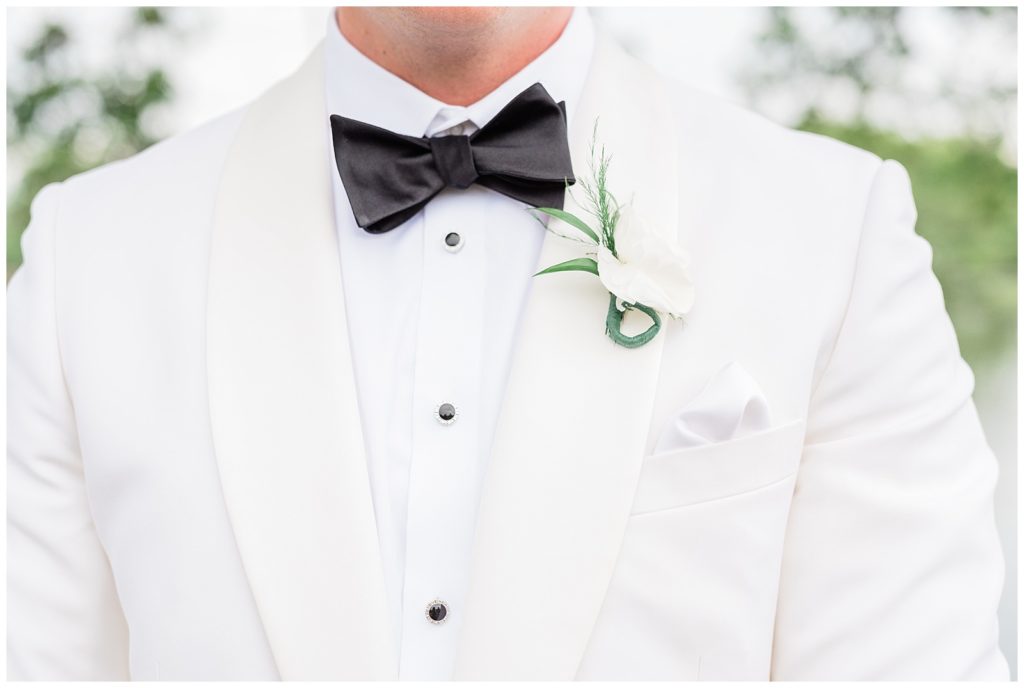 Groom wearing a white tux with a black bowtie and white boutonniere flower.