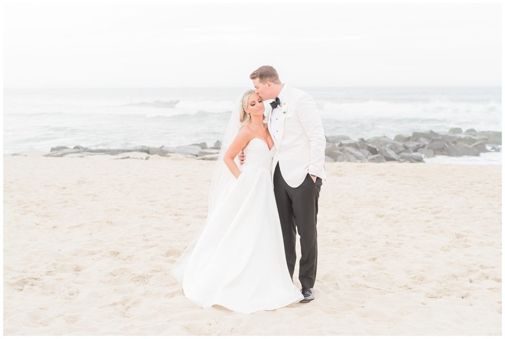 The groom kisses the bride on her head on the beach.