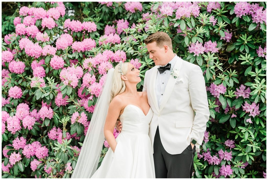 The bride and groom pose in front of a rhododendron bush.