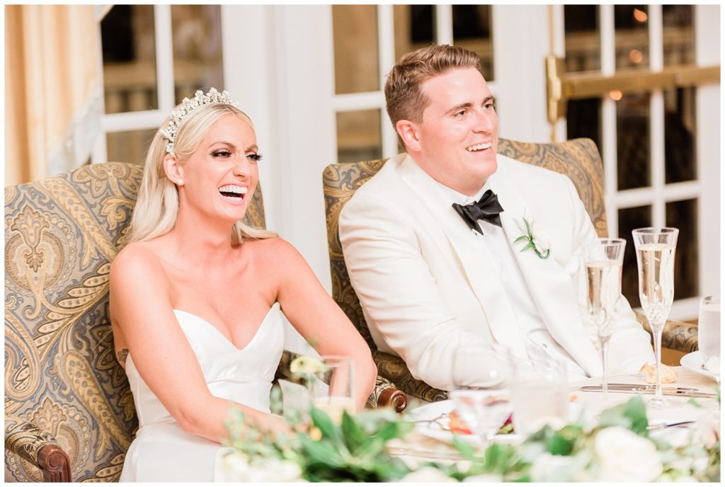 Bride and groom laugh during speeches at their wedding.