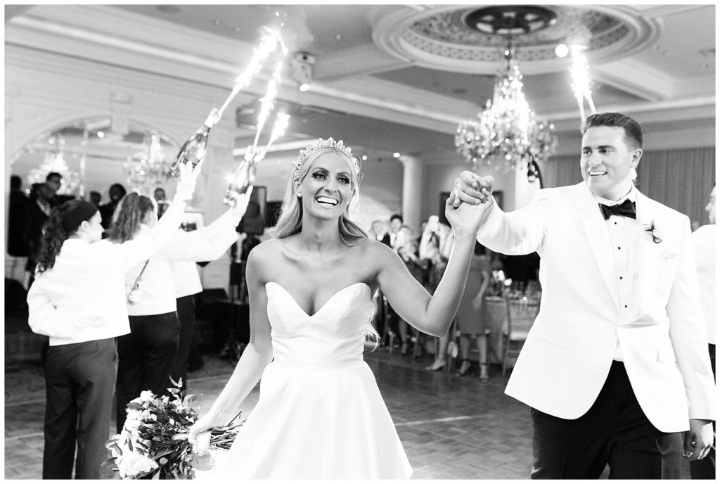 The bride and groom hold hands as the make their entrance to their reception through sparkler bottles of champagne.