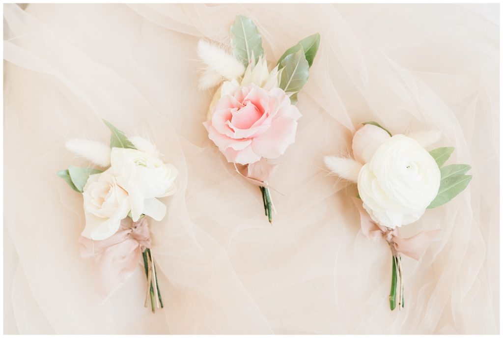 Pink and cream boutonnieres are styled on a piece of fabric.