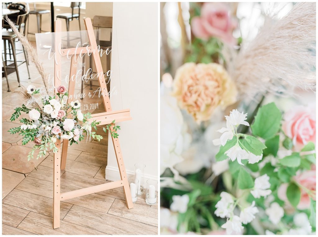 A clear acrylic welcome sign with white calligraphy sits on an easel with florals in the corner.