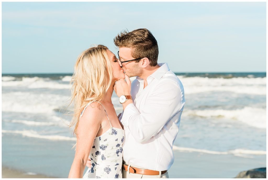 Ryan and Kristin stand facing each other, kissing in front of the crashing ocean waves. 