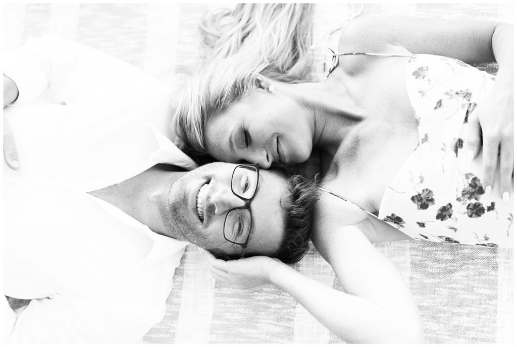 A black and white photo of Kristin and Ryan laying in opposite directions. The close angle shows their faces side by side, with Kristin's hand pressed against the side of Ryan's face. 