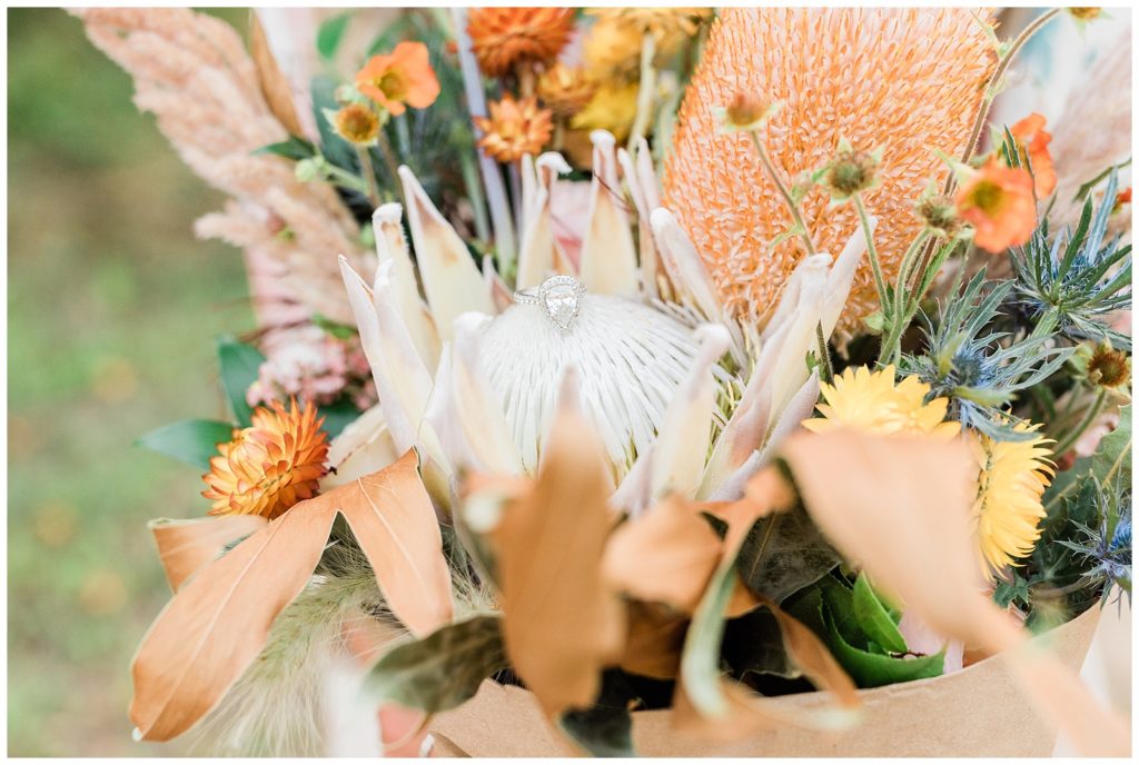 A close up photo of a beautiful fall colored bouquet, with various yellow and orange flowers with white decorative ribbons. 