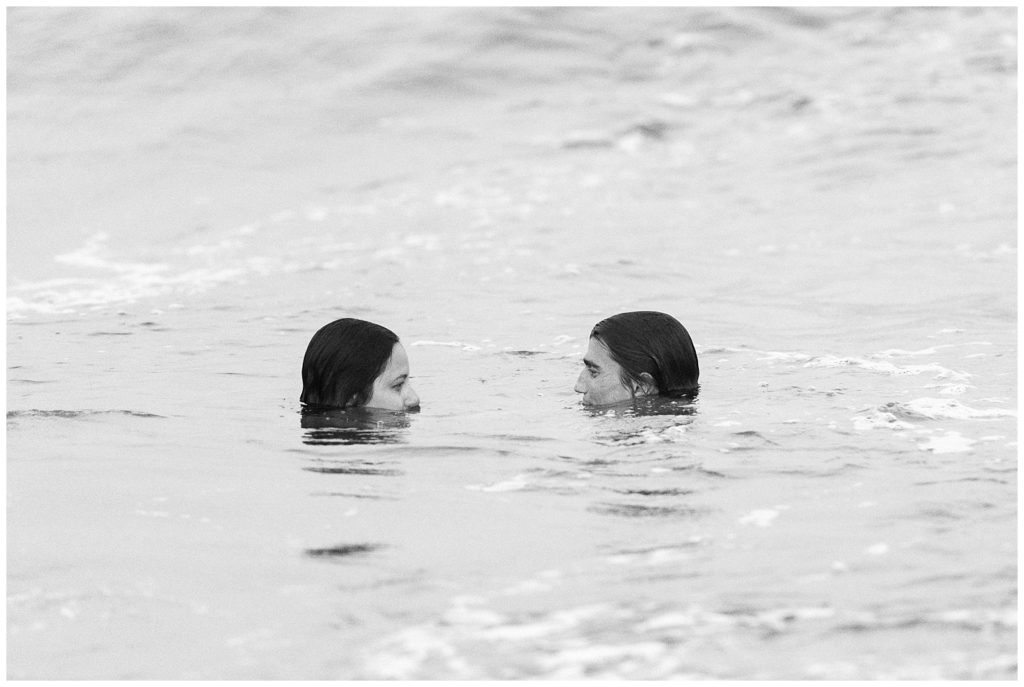 A black and white image of just Thiana and Brandon's heads in the ocean. The rest of their bodies are under water. 