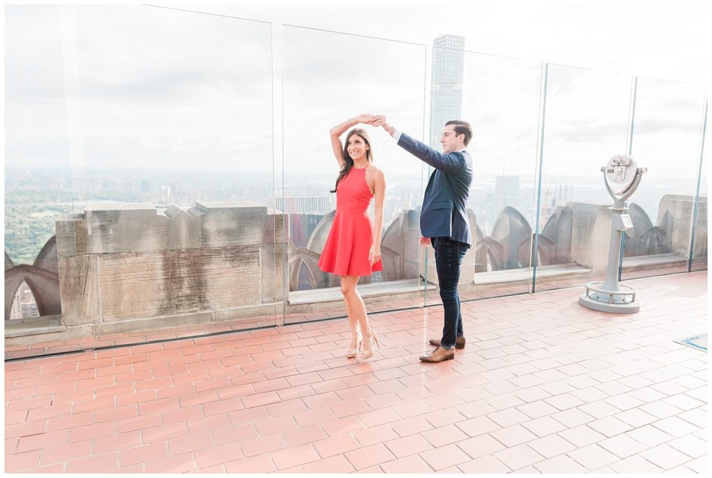 On "Top of the Rock" you can see the city skyline in the background. Nicole holds her hand up over her head. Mike, behind her, is reaching up and taking her hand almost as if they were mid dance. 
