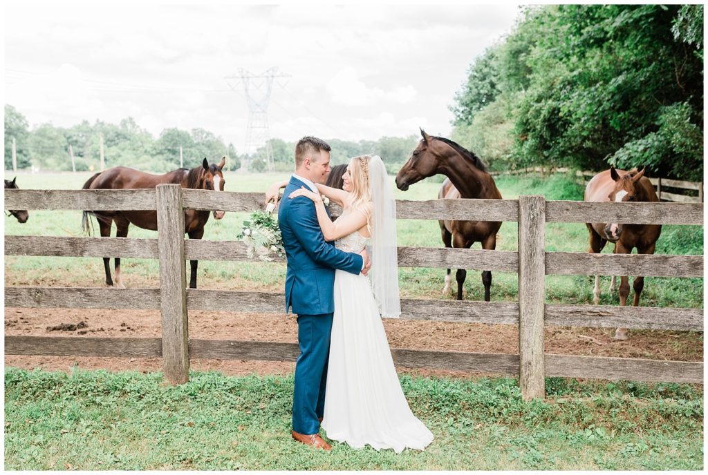 A bride and groom hold onto each other in front of a field of horses at Sterlingbrook Farm wedding venue in NJ.