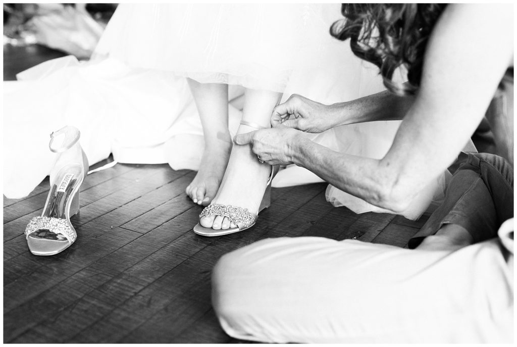 a close up of a woman kneeling on the ground closing the strap to Jillian's shoe; black and white image. 