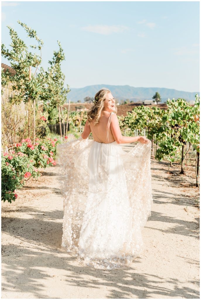 A bride laughs in the sunshine while holding her skirt and walking through the vineyards at Avensole Winery in Temecula, CA.