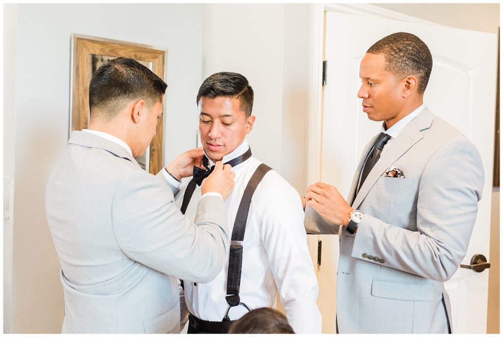 A groomsmen adjusts the groom's bowtie inside the groom suite at Avensole Winery wedding venue in Temecula.