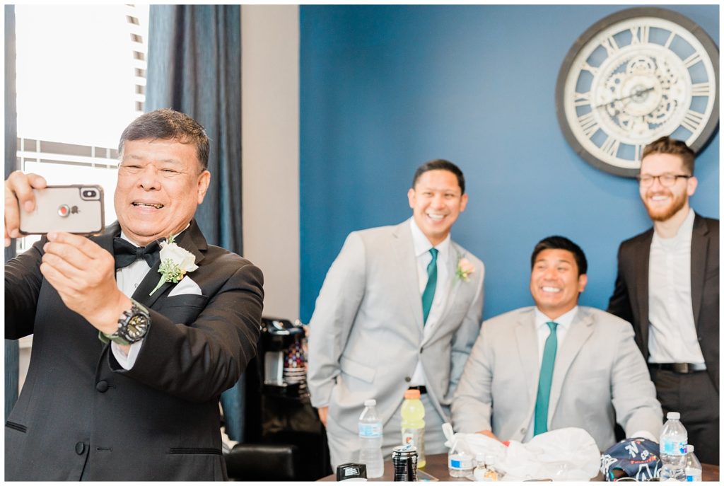 The groom's father takes a selfie with the groomsmen in the groom suite at Avensole Winery wedding venue in Temecula.