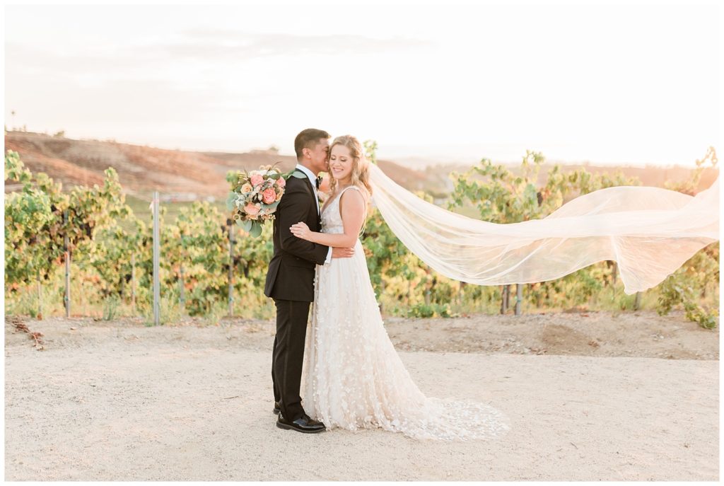 Bride and groom pose for a photo in front of the vineyards at golden hour at Avensole Winery, in Temecula, California.