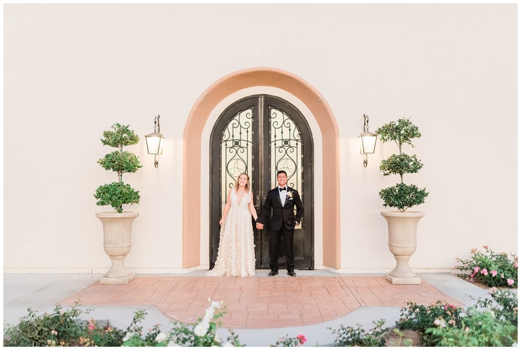A bride and groom hold hands in front of the doors of the Avensole Winery Wedding venue in Temecula, California.