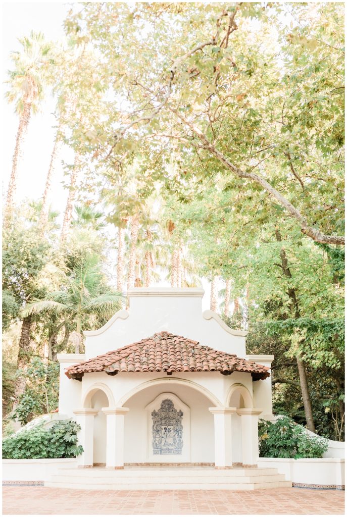 The iconic white stucco and marble theater stage with a blue and white hand-painted mural in the El Teatro area at Rancho Las Lomas, sits below towering palm and sycamore trees, captured by Orange County wedding photographer.