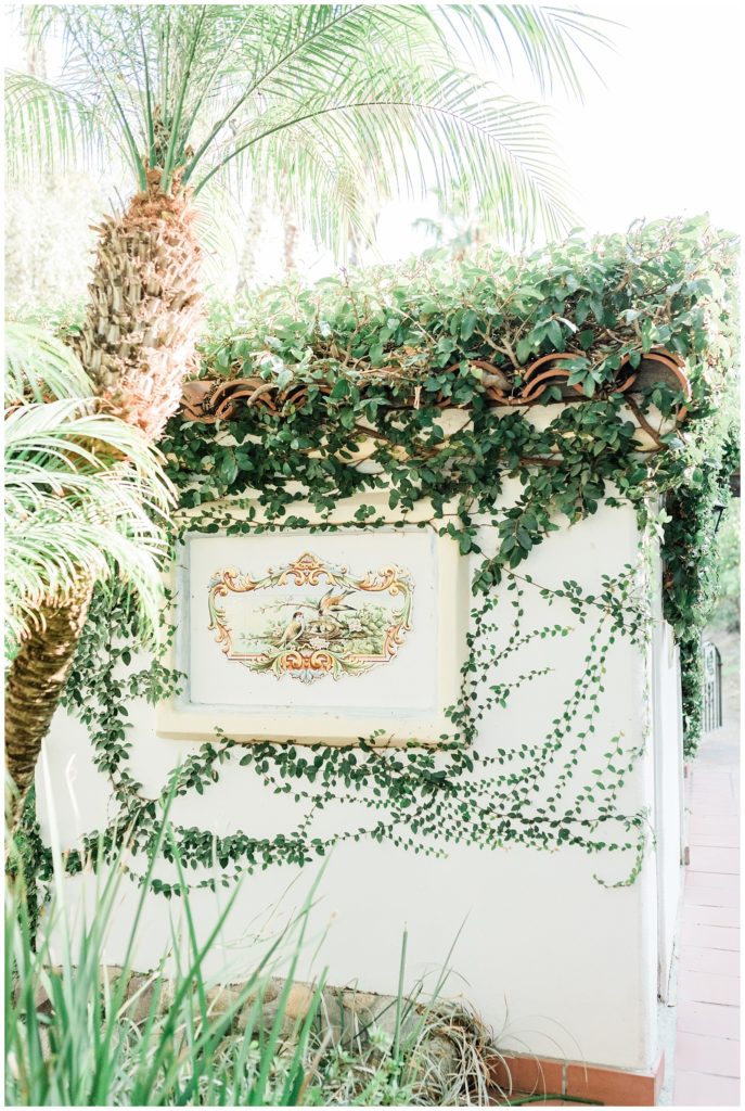 Green vines grow on the side of a white stucco building with a hand painted mural at Rancho Las Lomas open-air wedding venue in Southern California.