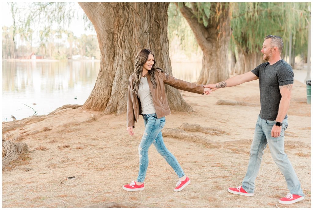 A couple holds hands walking by the lake for their engagement session in Riverside, California at Fairmount Park.