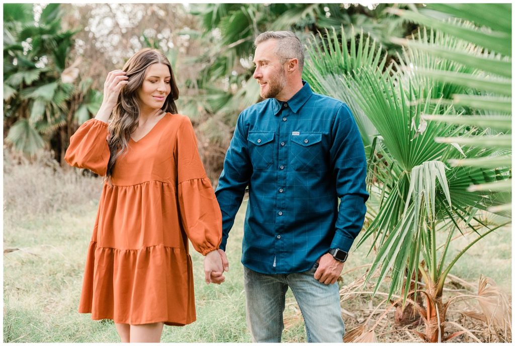 Engagement photos showing a couple holding hands in front of varieties of palm trees in the woods at Fairmount Park in Riverside, California.