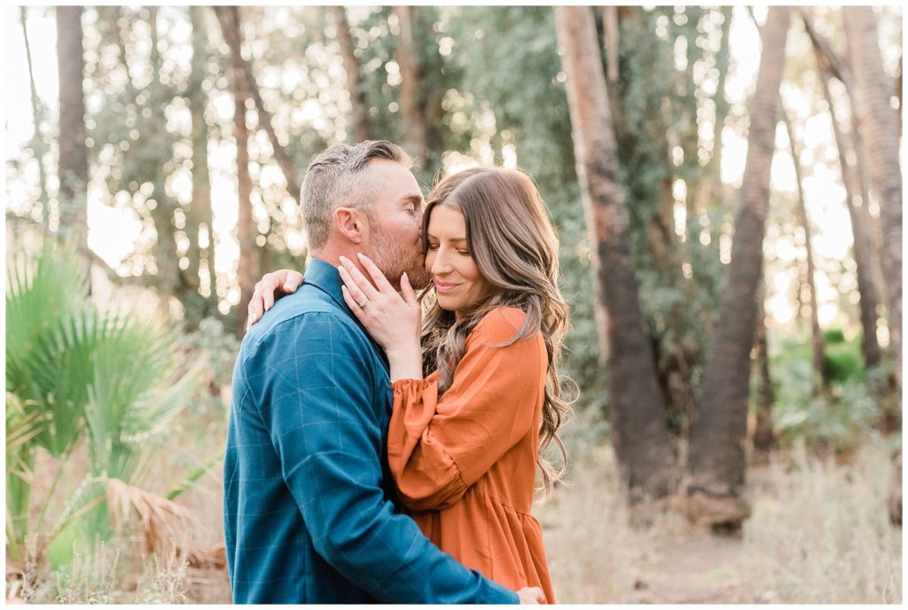 A man kisses his fiancee's cheek in the forest at Fairmount Park in Riverside, California.