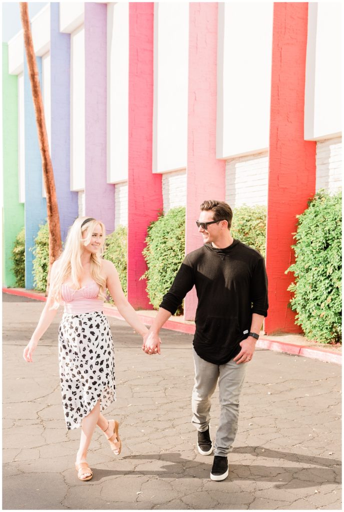 A couple holds hands walking during their Palm Springs California engagement session in front of the Saguaro Hotel.